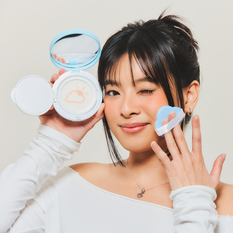 Model holding opened Dear Sun Perfecting SPF Cushion while winking