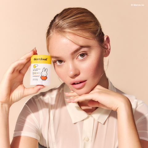 Model holding Miffy Sunny Defense Sun Stick SPF 50+ PA++++. Yellow cap with "dearcloud" logo. White packaging with Miffy character in orange dress. 