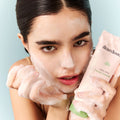 Model holding facial cleanser with bubble foam on hands and face