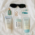 Flat lay of dearcloud sunscreen, sun stick, and hair clips, next to a pair of sunglasses and gold earrings.