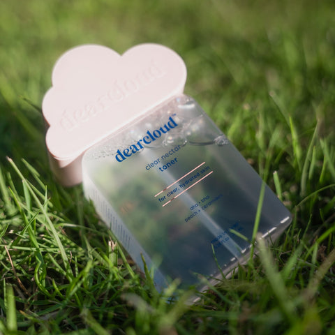 Clear toner bottle with pink cloud shaped dearcloud logo embossed lid. Front of bottle has "Clear Nectar Toner", "For Clear, Hydrated Skin", "AHA, BHA, Peach plus Ceramides", "Made in Korea", net weight of "5.24 FL OZ / 155 ML", and dearcloud logo in blue text color. Actual toner liquid color is clear.