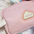 Closeup of a baby pink makeup bag and a white cloud on the bag with the logo "dearcloud" written in the cloud. A hand pis putting in a SPF stick into the bag. 