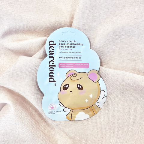 Packaging for a dearcloud beary cherub face mask featuring a cartoon bear with wings. Cloud shaped pouch on taupe linen fabric. 