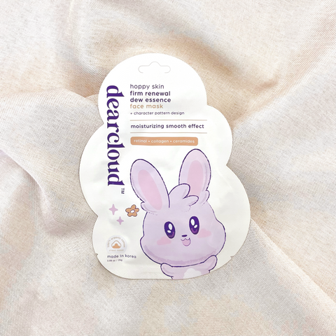 dearcloud Hoppy Skin Firm Renewal Dew Essence face mask with a cute bunny character. Yellow cloud-shaped packaging with a light pink bunny character. Pouch is on a taupe linen fabric. 