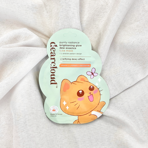 Front of the dearcloud Purrty Radiance face mask cloud-shaped packaging, showing a cartoon cat with its tongue sticking out and product details. Pouch is on a taupe linen fabric.